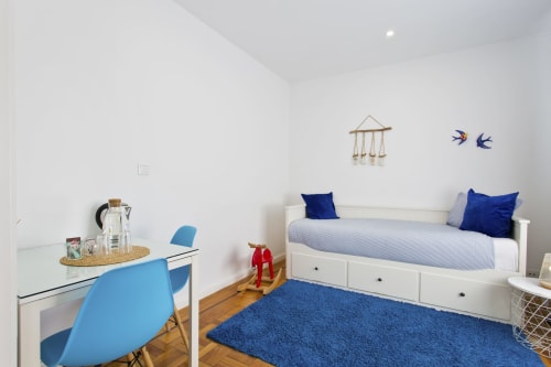 Chambre moderne de la Pension Cem Contos Porto avec lit blanc, accents bleus, coin bureau et parquet