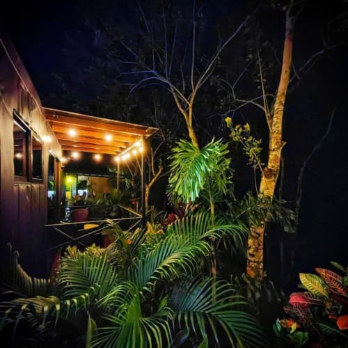Patio nocturno del Contenedores Boutique Hotel con pérgola de madera iluminada, plantas tropicales y diseño moderno en contenedores