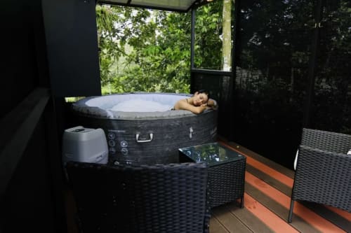 Huésped relajándose en bañera de agua caliente al aire libre en Contenedores Boutique Hotel, Costa Rica, rodeado de exuberante vegetación