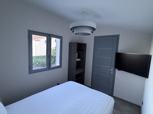 Chambre moderne à la Villa Monaco, SNC Blue Vista Beausoleil, avec lit, TV écran plat, porte noire, luminaire suspendu et vue sur mer