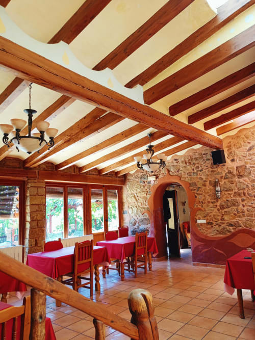 Comedor rústico en Posada del Río Carbo con vigas de madera vista, muros de piedra y manteles rojos