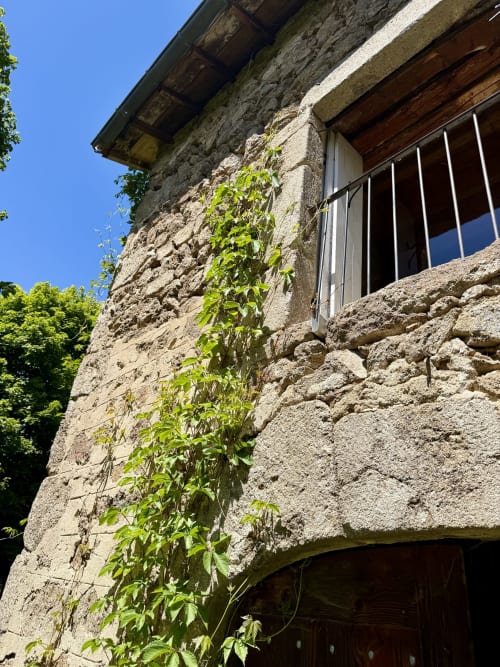 Façade de villa en pierre historique au 1830 à Églisolles, aux murs couverts de lierre, fenêtre barreaudée et ciel dégagé