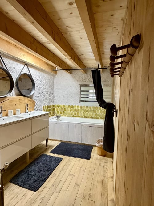 Salle de bains moderne de la villa Le 1830 avec poutres en bois, carrelage hexagonal jaune, vasque blanche et vue sur jardin à Églisolles