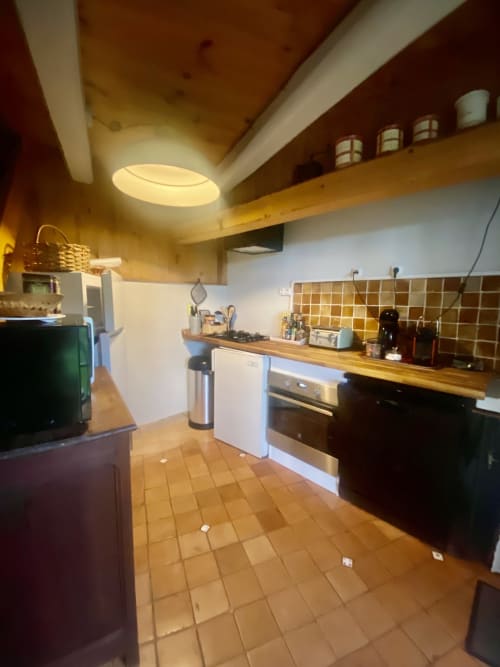 Cuisine moderne de la villa Le 1830 à Églisolles avec plans de travail en bois, électroménagers inox et carrelage en terre cuite