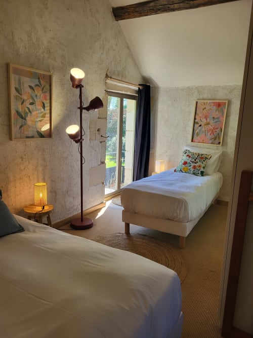 Bright bedroom at Domaine Des Forges De La Vache with two white beds, floral artwork, and garden view through glass doors