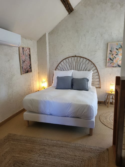 Cozy bedroom at Domaine Des Forges De La Vache cottage in Raveau with woven headboard, white bedding, and ambient lighting
