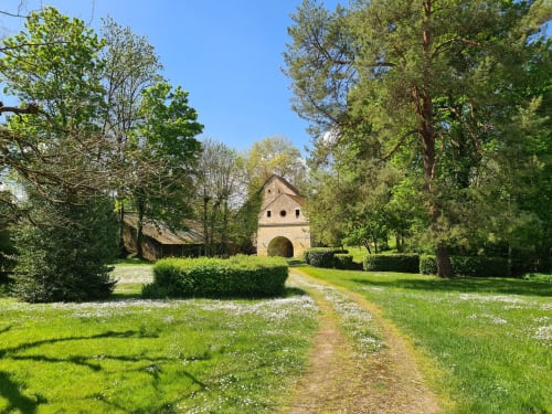 Tree-lined pathway leading to historic stone cottage at Domaine Des Forges De La Vache in Raveau, France
