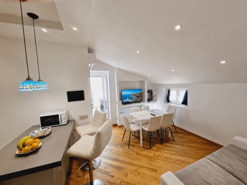 Modern luxury apartment in Sanremo with open-plan dining and living area, white furnishings, wooden floors, and city views