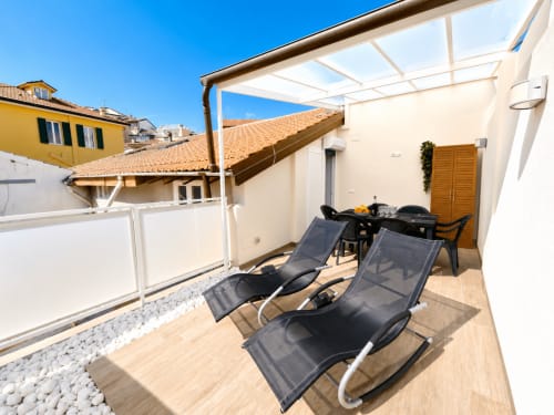 Terrasse ensoleillée de l'appartement de luxe HomeholidaySanremo à Sanremo avec transats, coin repas et vue sur la ville