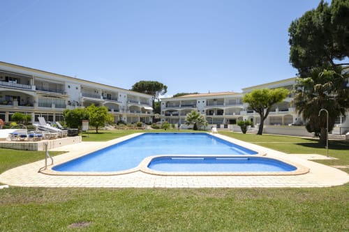 Complexo de apartamentos RB Algarve com piscina, espreguiçadeiras, jardins exuberantes e edifícios brancos em Vilamoura