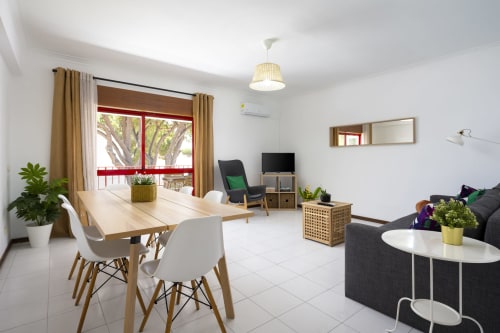 Apartamento moderno e luminoso no RB Algarve com mesa de jantar, sofá, TV, cozinha e amplas janelas com vista para a piscina