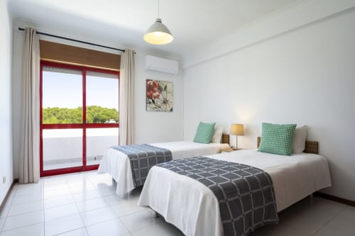 Apartamento DINIS em RB Algarve Vilamoura: quarto twin luminoso com portas de varanda vermelhas com vista para a piscina, comodidades modernas e