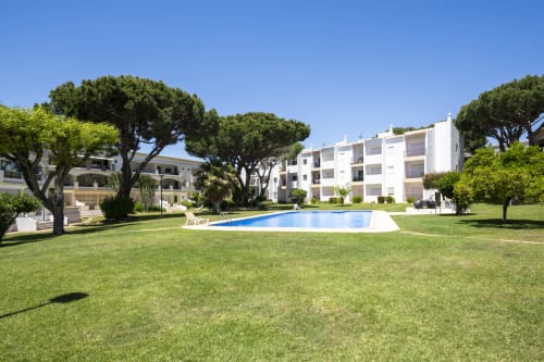 Vista da piscina do apartamento RB Algarve com jardim paisagístico, piscina azul e modernos edifícios brancos cercados por árvores