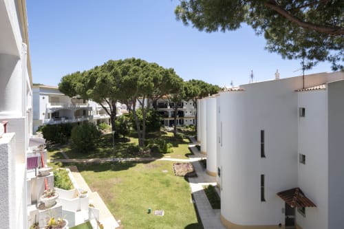 Pátio do hotel RB Algarve em Vilamoura com jardim verdejante, árvores altas e edifícios brancos de apartamentos sob céu claro