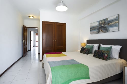 Quarto brilhante na RB Algarve Vilamoura com cama queen, manta colorida, guarda-roupa em madeira escura e comodidades modernas