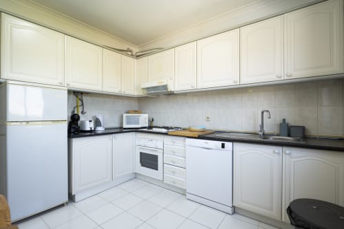 Cozinha moderna no apartamento DINIS do RB Algarve Vilamoura com armários brancos, bancadas pretas e aço inoxidável
