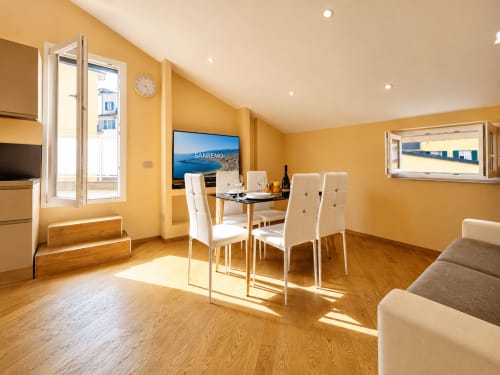 Séjour lumineux jaune vif avec table à manger, chaises blanches et vue sur balcon à l'hôtel Sanremo