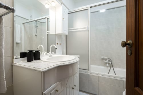 Banheiro moderno no apartamento DINIS do RB Algarve Vilamoura com lavatório branco, pia redonda, espelho e box de vidro.