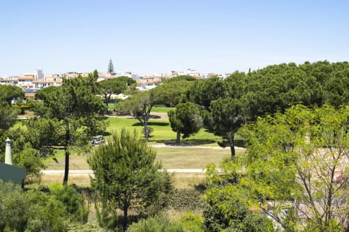 Vista panorâmica do RB Algarve em Vilamoura, Portugal com paisagismo exuberante, árvores e edifícios ao fundo sob céu limpo