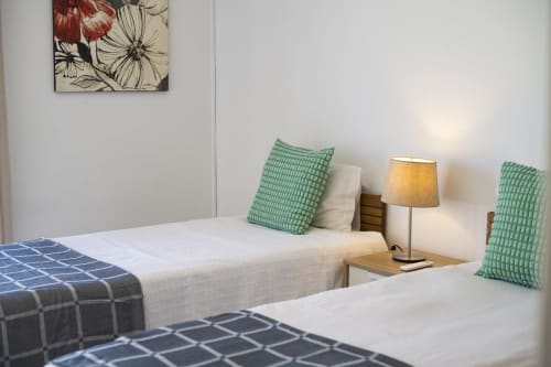 Quarto moderno do hotel RB Algarve com duas camas, almofadas com padrão verde, luminária de cabeceira e arte floral nas paredes em Vilamoura