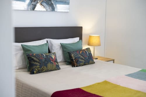 Quarto moderno no RB Algarve Vilamoura com cabeceira escura, almofadas verdes estampadas, roupa de cama branca e luminária amarela acesa