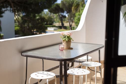 Varanda do quarto PEDRO em RB Algarve com mesa, bancos, vasos de flores e vista para o jardim