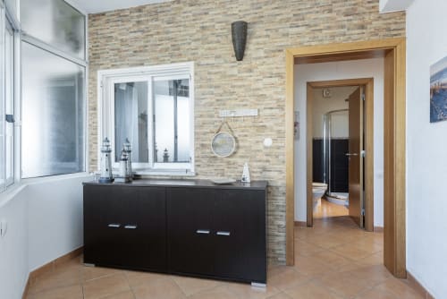 Entrada moderna do apartamento em RB Algarve Vilamoura com parede de tijolos, guarda-roupa preto, portas de madeira e piso em azulejos.
