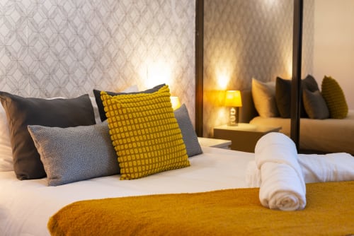 Quarto de luxo do hotel RB Algarve com almofadas amarelas, roupa de cama branca, toalhas enroladas e decoração moderna