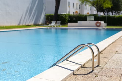 Piscina com corrimãos de metal no hotel RB Algarve em Vilamoura, Portugal, com água azul e edifício branco