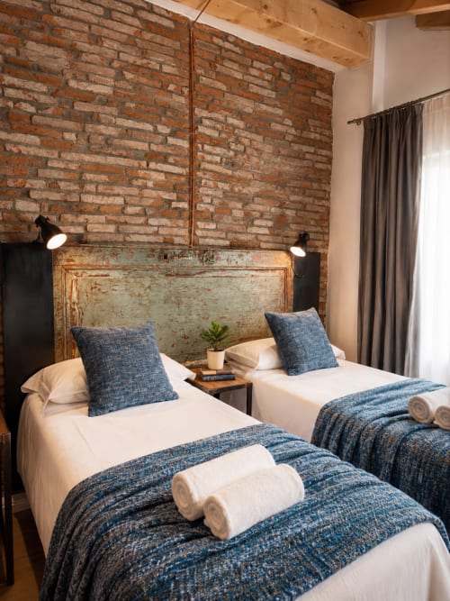Camera da letto in stile loft a Bergamo con muro in mattoni a vista, due letti con tessuti blu e illuminazione a sospensione