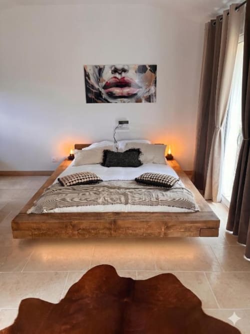 Chambre moderne du Mas Aurel de Provence avec lit plateforme en bois, linge blanc, coussins décorés et art mural contemporain