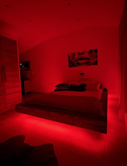 Chambre moderne éclairée d'une lumière rouge ambiante au Mas Aurel de Provence, avec lit garni de coussins et œuvres d'art murales à Peypin,