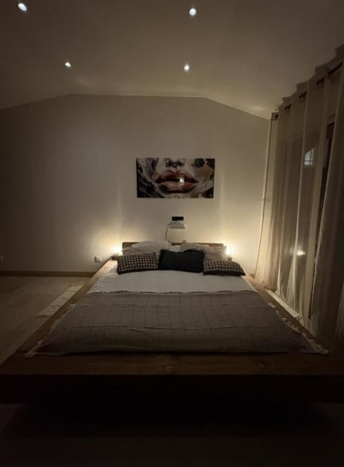Chambre moderne au Mas Aurel de Provence avec lit queen-size, éclairage ambiant, œuvres murales et rideaux offrant vue sur le jardin à Peypin