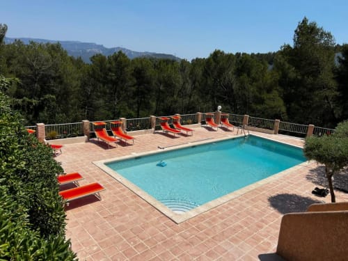 Piscine de villégiature aux eaux bleues, chaises longues rouges et montagnes boisées du Mas Aurel de Provence à Peypin