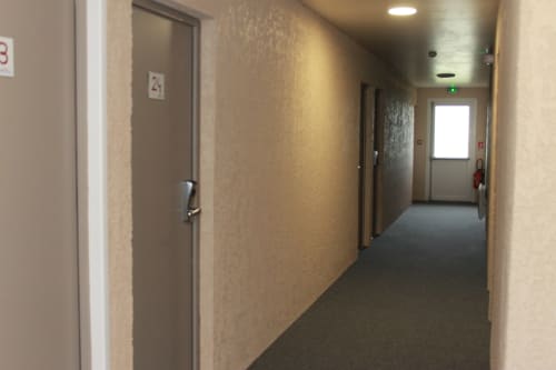 Couloir de l'Hôtel Libre à La Vespière avec portes numérotées, murs beige neutre et éclairage encastré menant à la sortie
