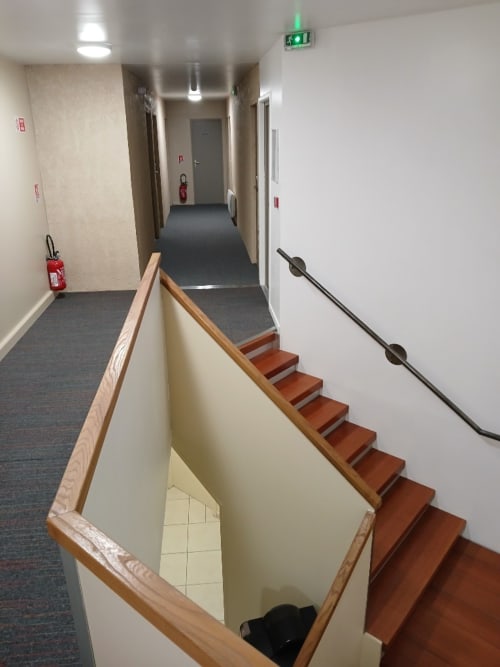 Escalier intérieur de l'Hôtel Libre avec rampes en bois, marches rouges et couloir menant aux chambres d'hôtes avec sortie de secours
