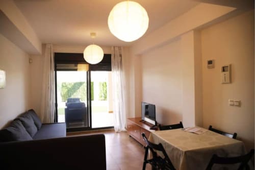 Séjour moderne avec coin repas, téléviseur écran plat, luminaires circulaires au plafond et portes vitrées donnant sur terrasse