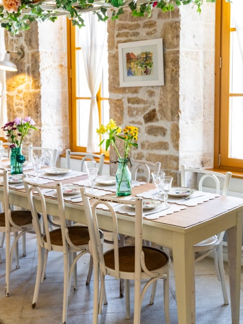 Elegant dining room at La Maison George with stone walls, cream chairs, and fresh flowers in green vases