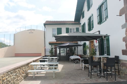 Auberge Etchoinia terrace with black umbrellas, seating, and white building facade in Lasse, France