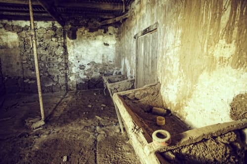 Habitación rústica abandonada en Hotel Rural El Cabo de Villaverde, España, con paredes deterioradas y vasijas de barro
