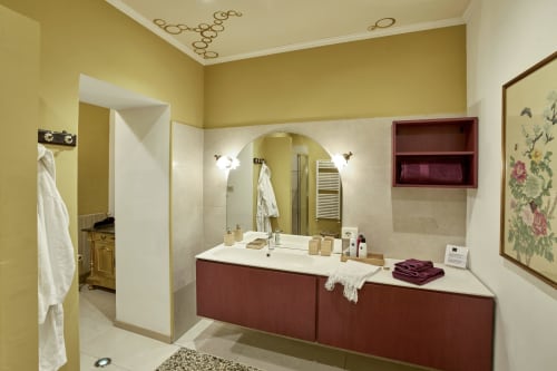 Bagno lussuoso con mobile borgogna, specchio ad arco, pareti gialle e dettagli marmo presso A Casa Armenia B&B Torino