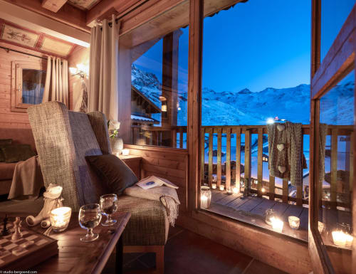 Balcon d'un appartement alpin luxueux au crépuscule, vue panoramique sur les montagnes enneigées, coin détente cosy et ambiance aux chandelles