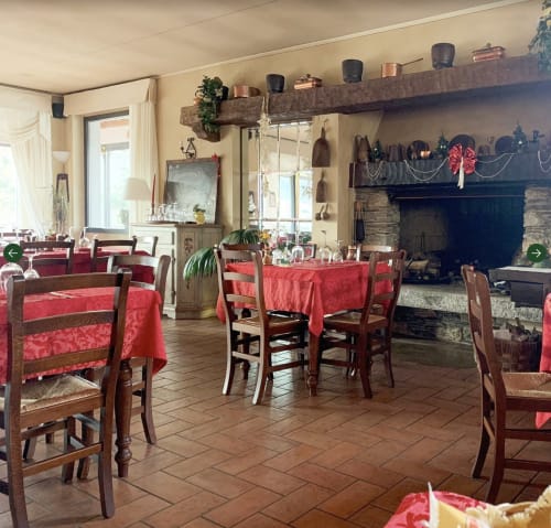 Sala da pranzo rustica con tovaglie rosse, sedie in legno, camino e finestre con vista sul lago presso il ritiro di lusso di Stresa.