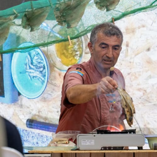 Chef del Hotel Rural El Cabo en Villaverde demostrando cocina tradicional con productos frescos y hierbas aromáticas colgantes
