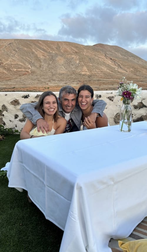 Tres personas sonriendo alrededor de una mesa blanca con flores, con un paisaje de montañas desérticas de fondo en Hotel Rural El Cabo, Villaverde