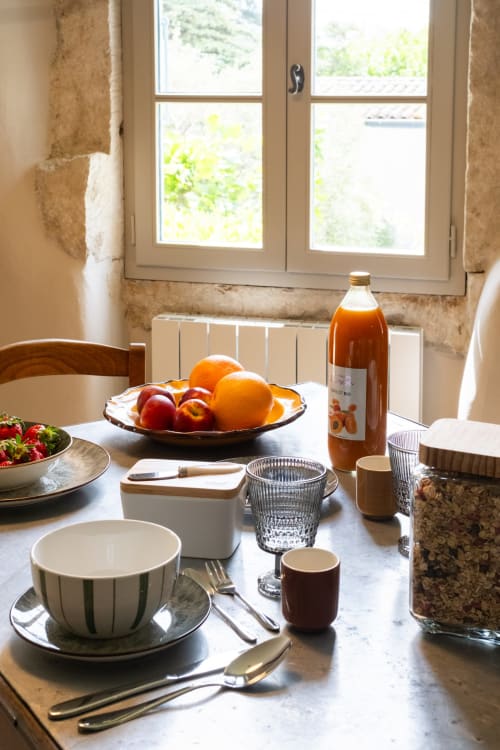 Sunny breakfast table at Le Jardin Secret cottage in Grignan with fresh fruit, juice, and place settings by large windows