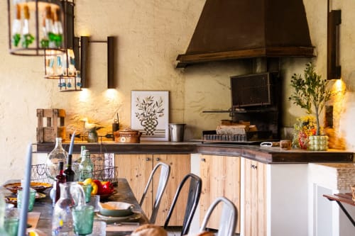 Rustic cottage kitchen at Le Jardin Secret in Grignan with wood cabinets, dining table, fireplace, and warm lighting.