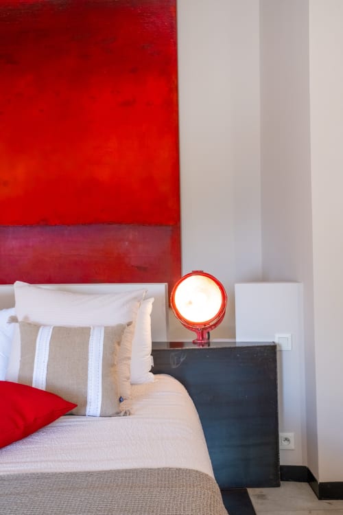 Modern bedroom with red accent wall, striped pillow, and red lamp at Le Jardin Secret cottage in Grignan