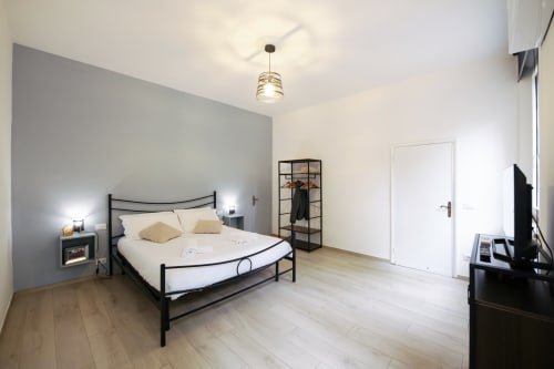 Modern bedroom at LikeHome Mentessi in Ferrara with black metal bed, gray accent wall, wooden floors, and city views