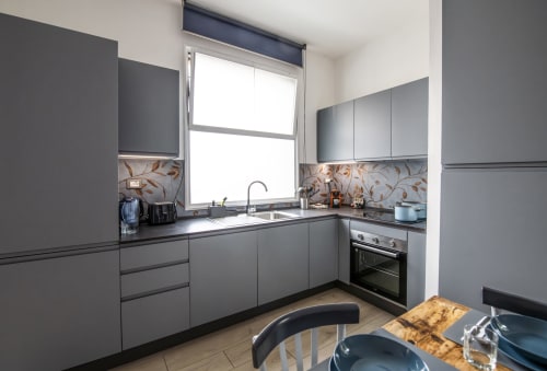 Modern gray kitchen with window, black countertop, stainless steel appliances in Ferrara apartment